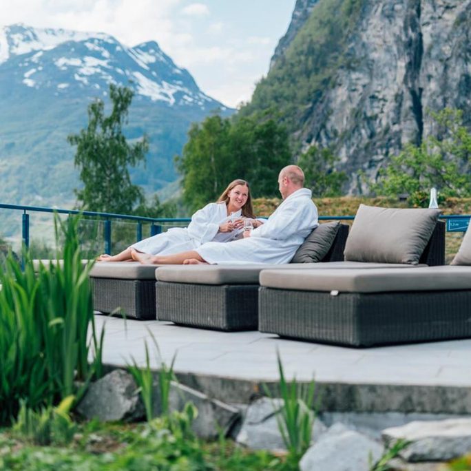 Guests relaxing on a fjord-side terrace below steep green mountains