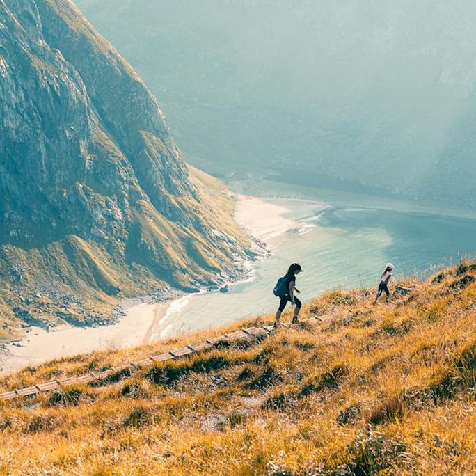 Two hikers crossing a golden ridge above a turquoise Arctic bay